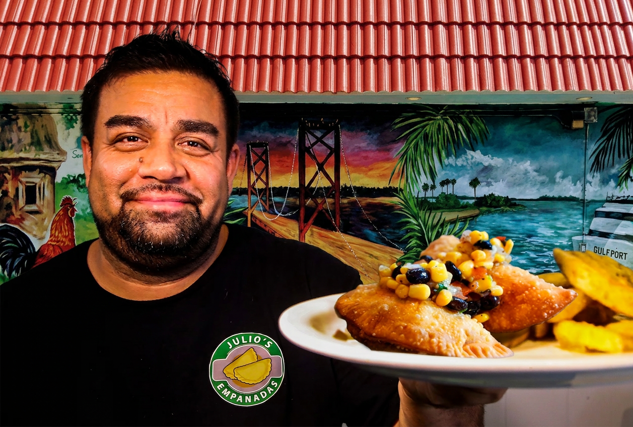 Julio, owner of Julio's Empanadas, holding a plate of food in front of his hand-painted Gulfport mural