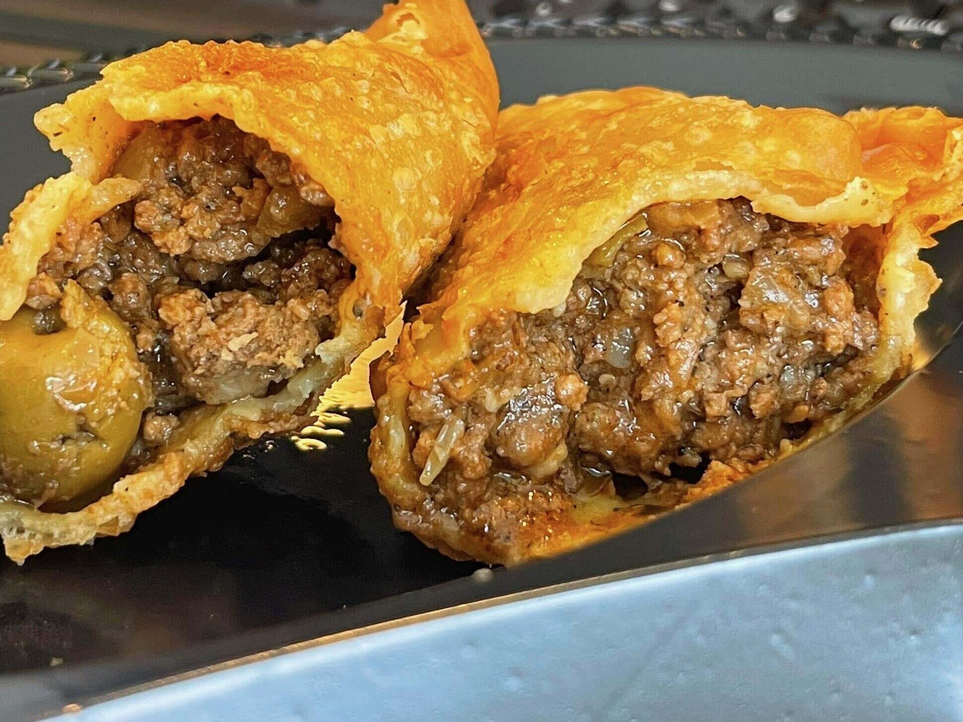 Beef empanada split open on a silver tray, revealing densely packed seasoned beef filling